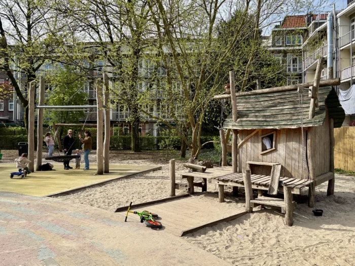 Wooden play house and nest swing on sunny day with trees and houses behind