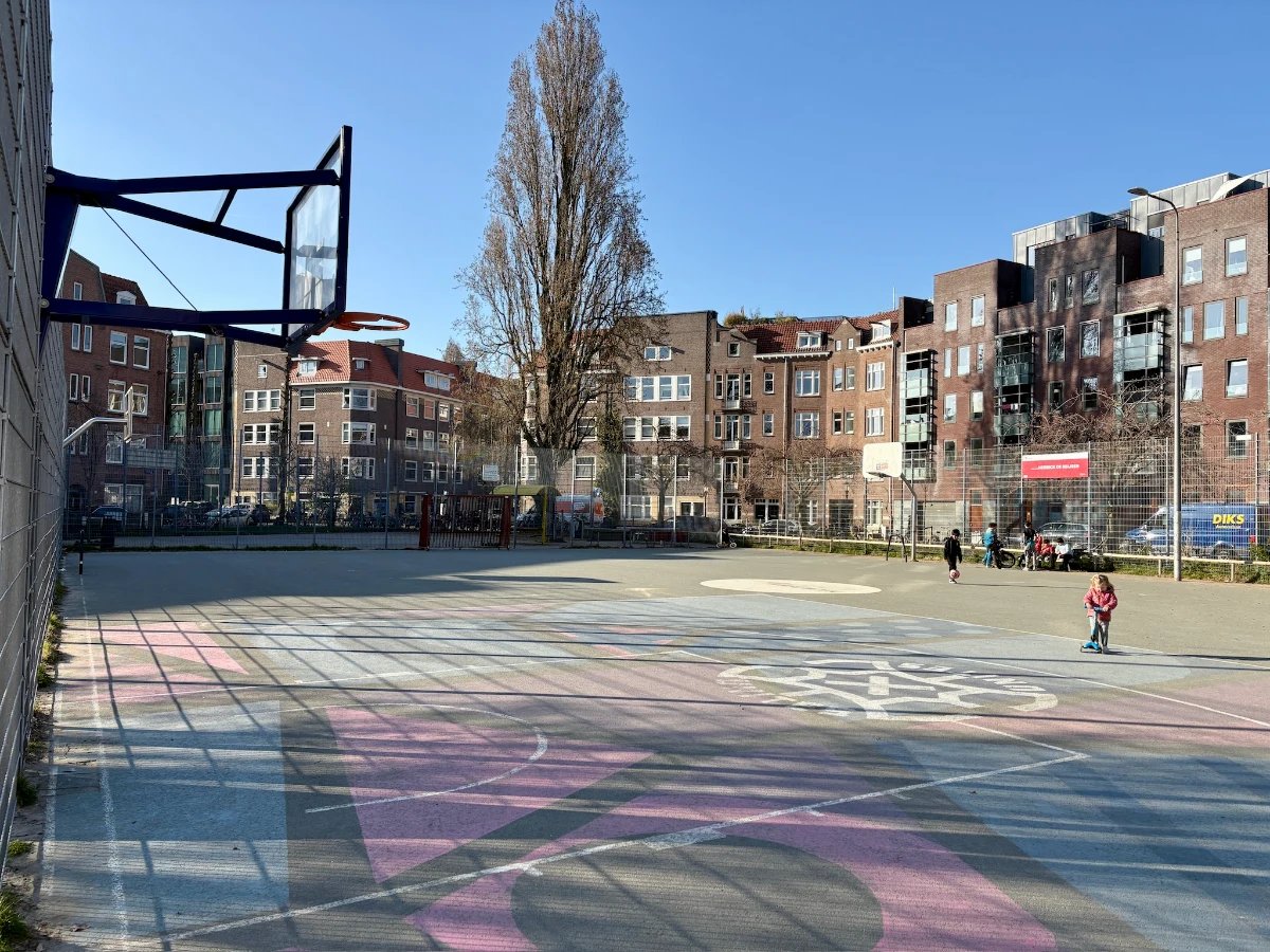 Toddler riding scooter on large open basketball court set in a residential plaza with red and blue shapes painted on the pavement
