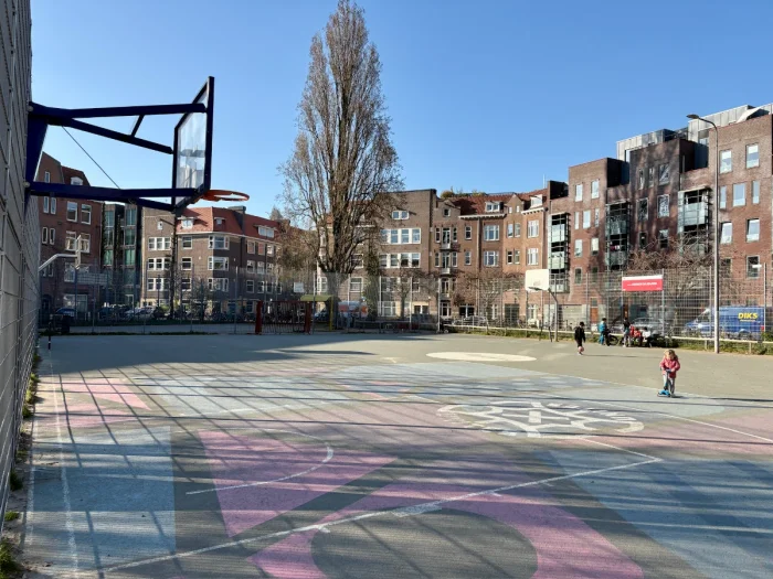 Toddler riding scooter on large open basketball court set in a residential plaza with red and blue shapes painted on the pavement