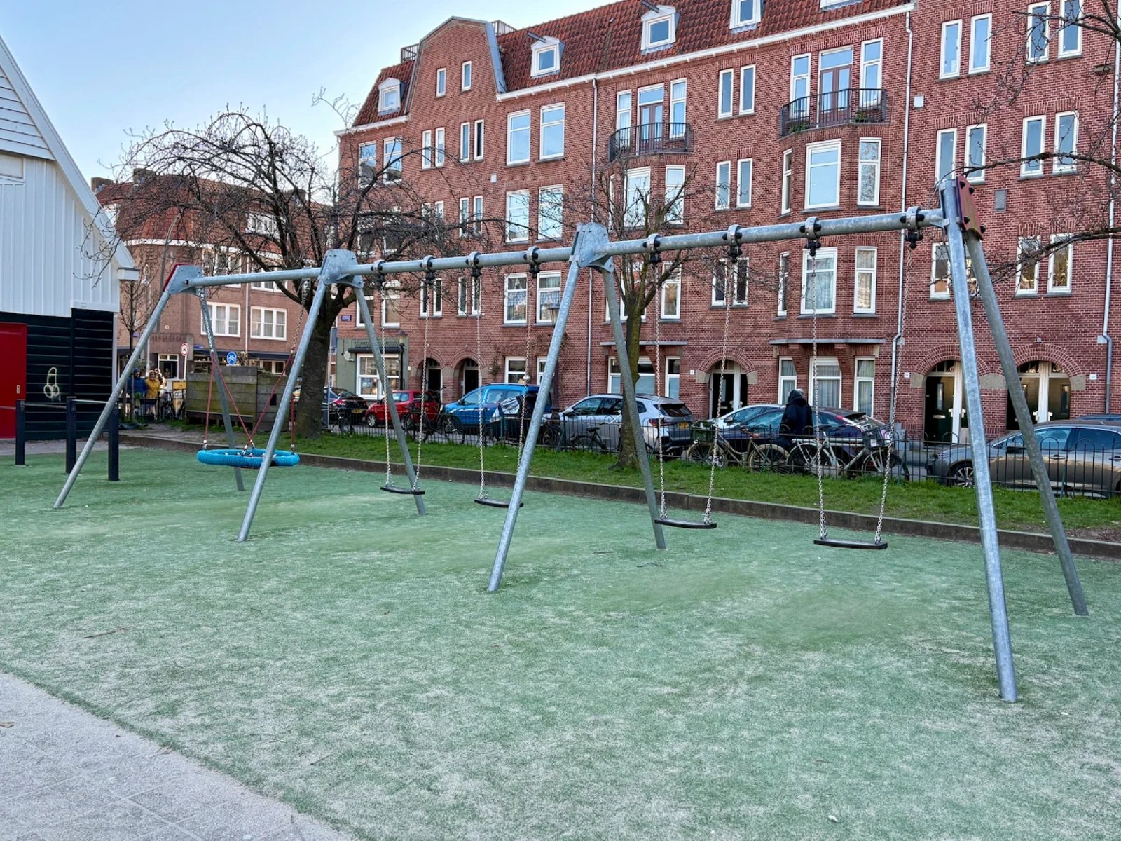 Large swing set with three swings and one nest swing with residential buildings behind