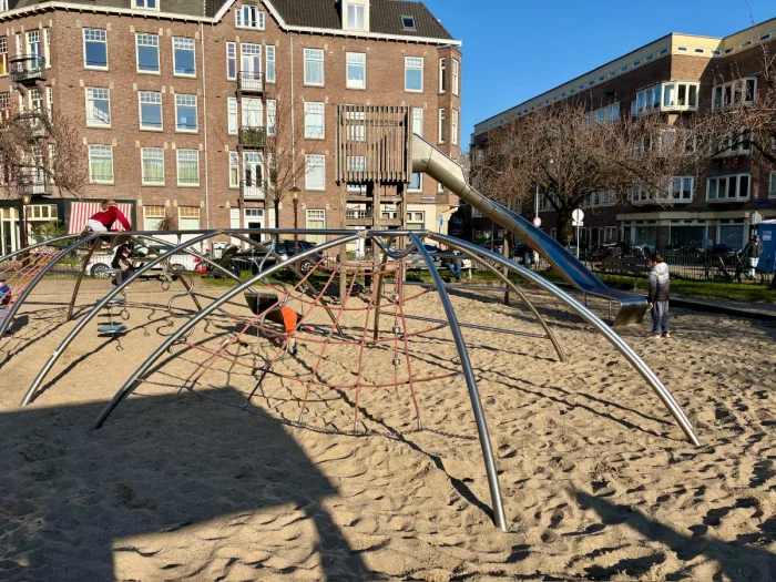Kids playing on metal and rope climbing frame with tall wooden tower and slide and residential buildings behind
