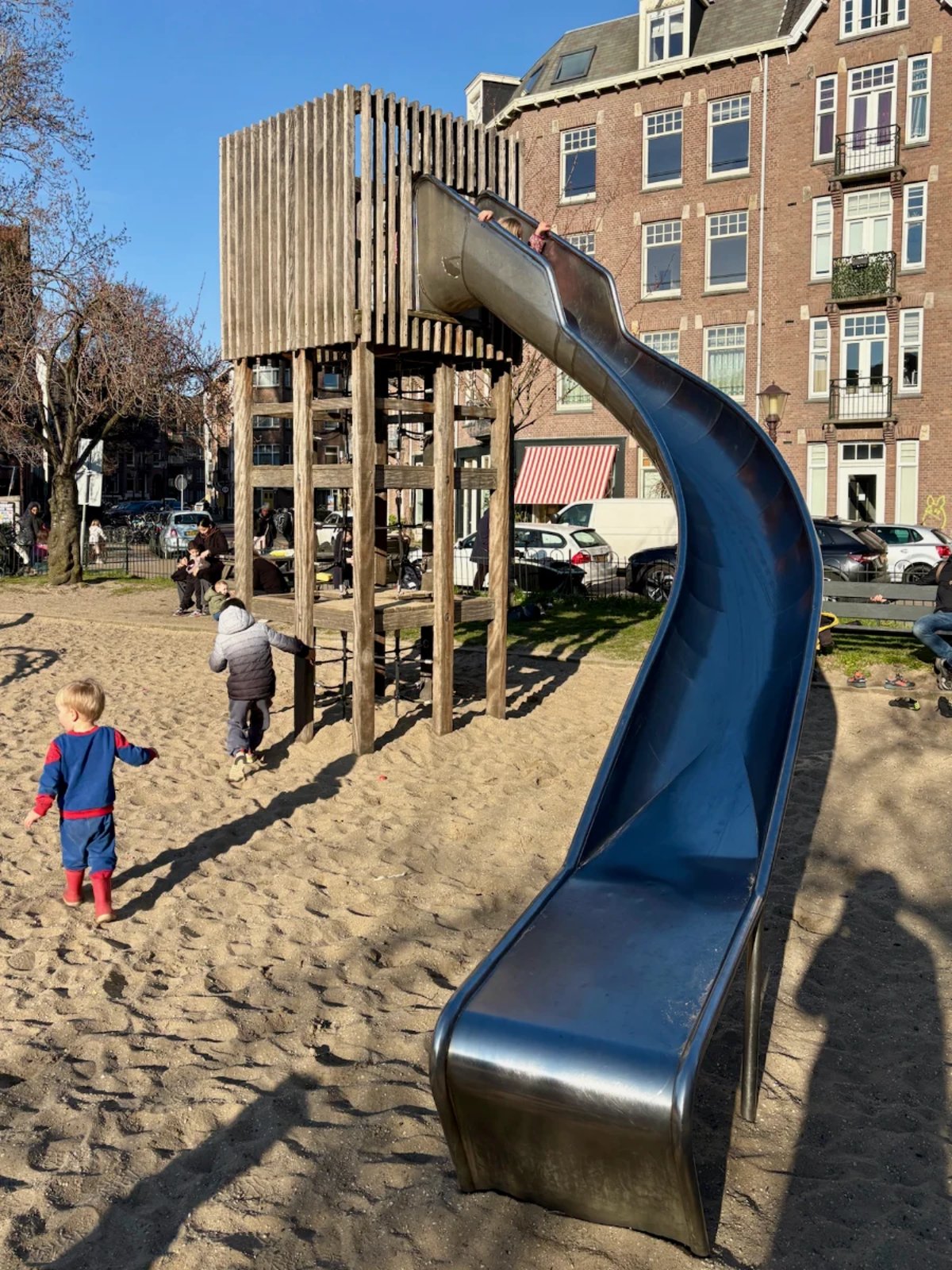 Kids playing on a tall wooden tower with curved metal slide set on sand