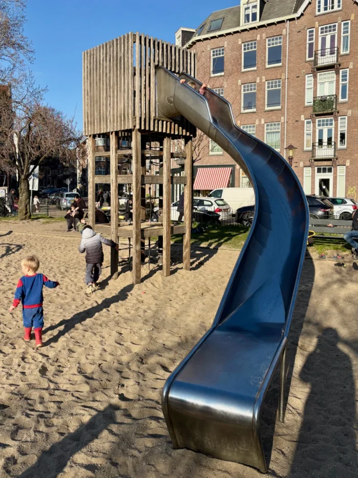 Kids playing on a tall wooden tower with curved metal slide set on sand