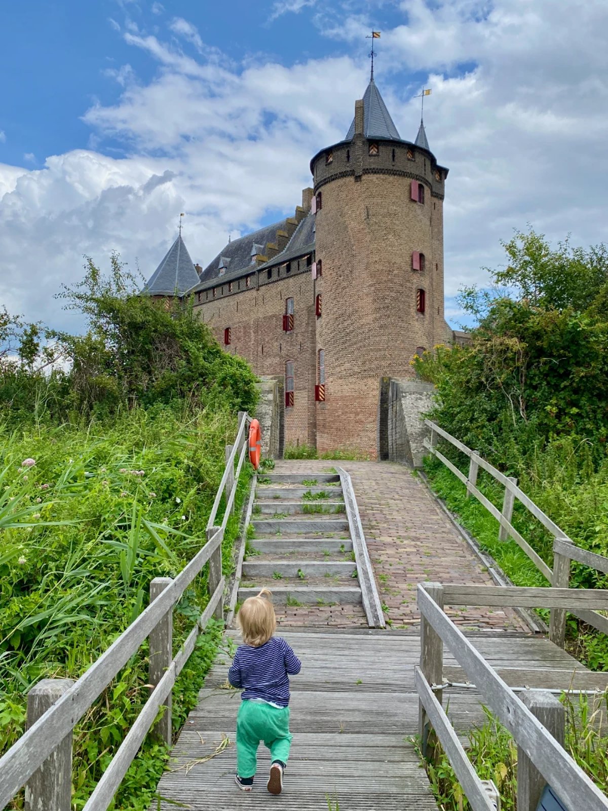 Child walking on pier toward stairs and a tall brick castle beyond