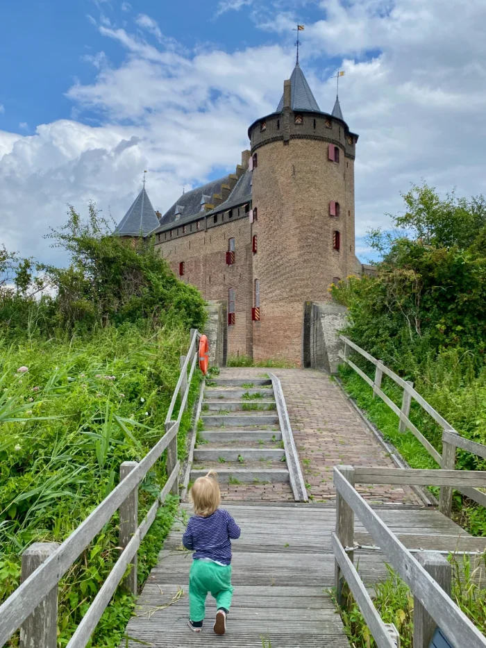 Child walking on pier toward stairs and a tall brick castle beyond