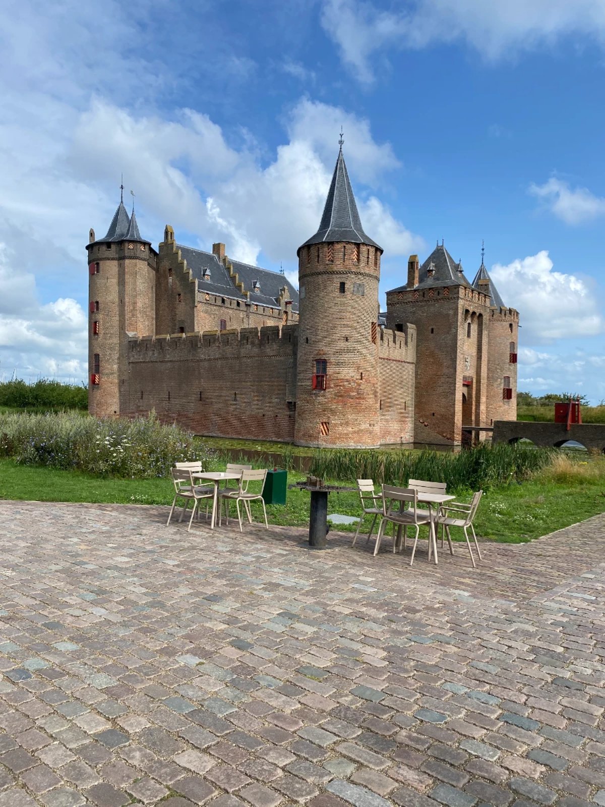 Brick castle with slate grey roof with dining tables and chairs in the foreground