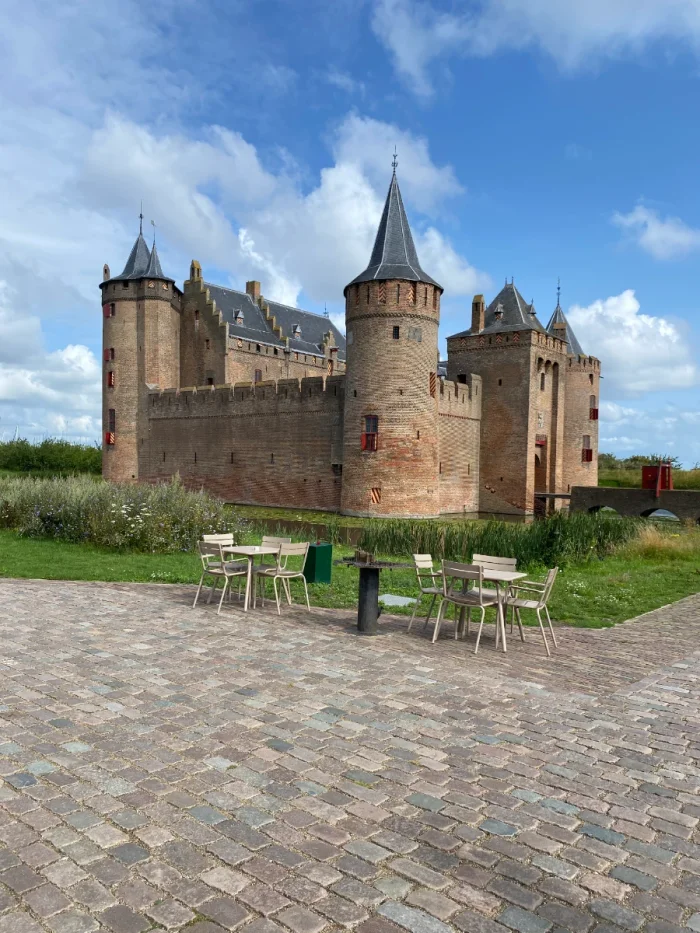 Brick castle with slate grey roof with dining tables and chairs in the foreground