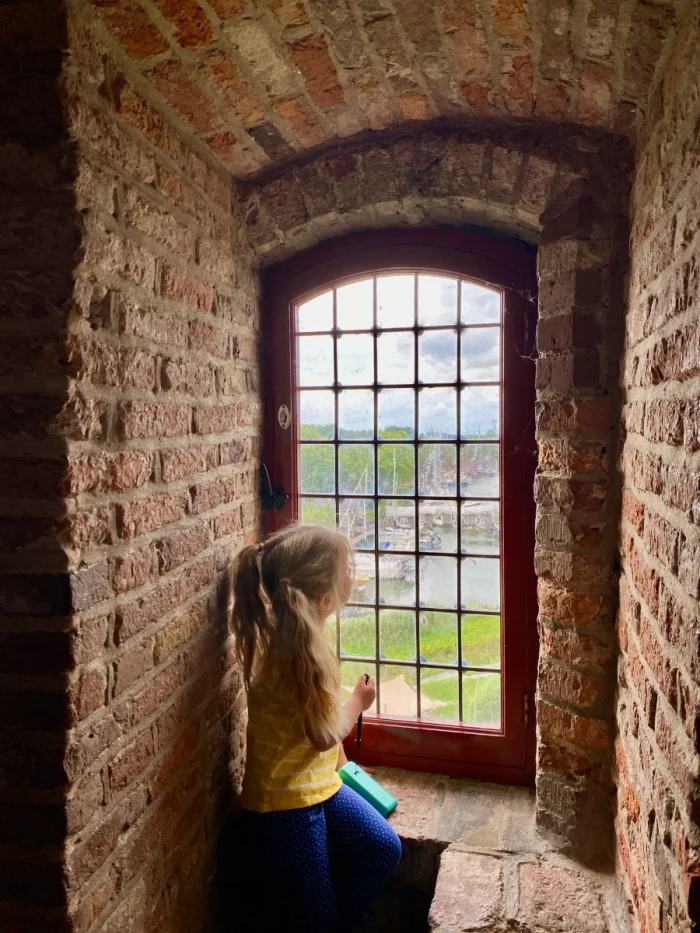 Girl looking out paned windows set within a thick brick castle wall