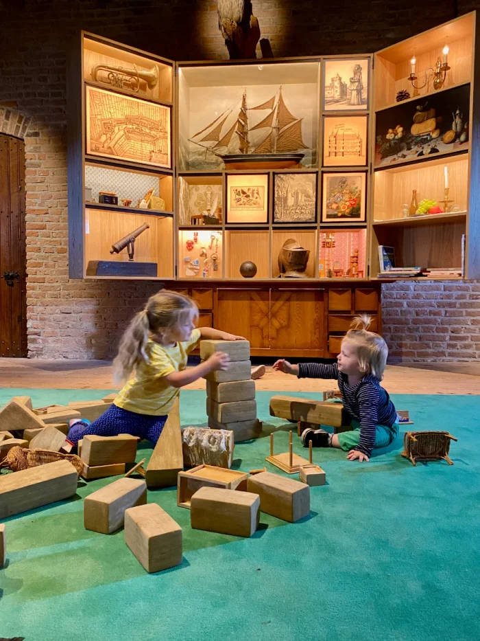 Children playing with toys on green rug with large curio cabinet and various medieval artifacts on display