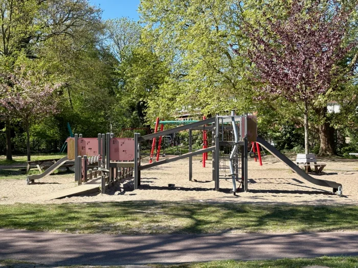 Playground structure with slides, ramps, and firepole with sand and spring trees around