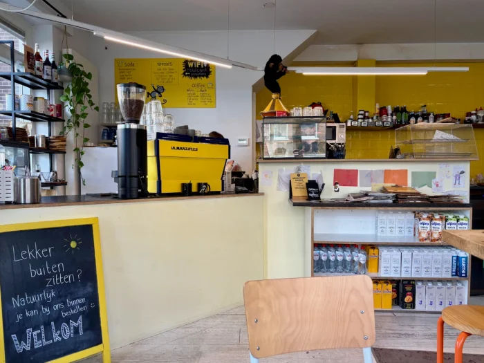 Yellow and white coffee shop counter with products for sale, yellow coffee machine, and yellow framed sandwich board