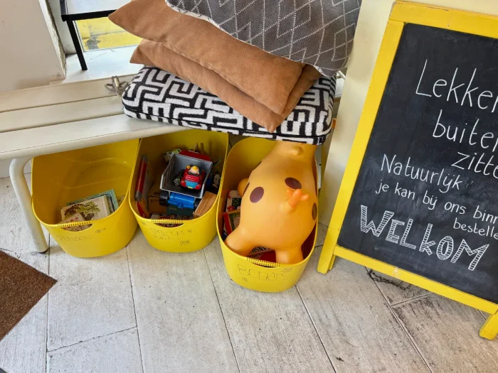 Yellow buckets with toys under a white bench with pillows