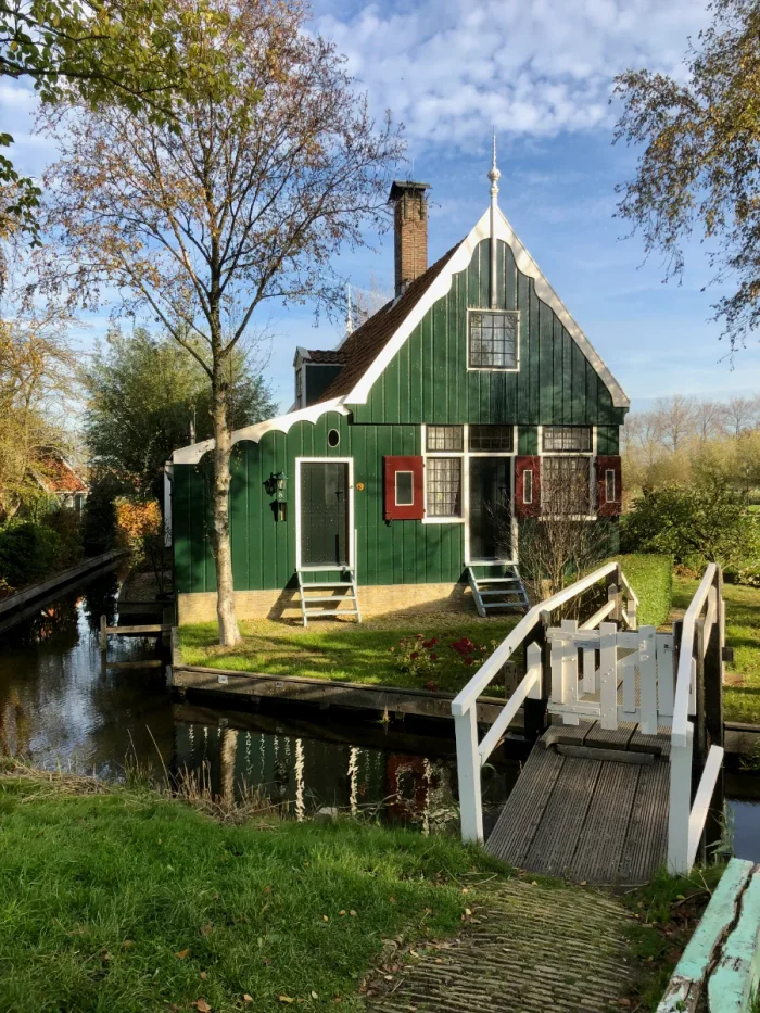 Zaanse style house painted green with red shutters, white trim, and set on a small grassy island with gated bridge