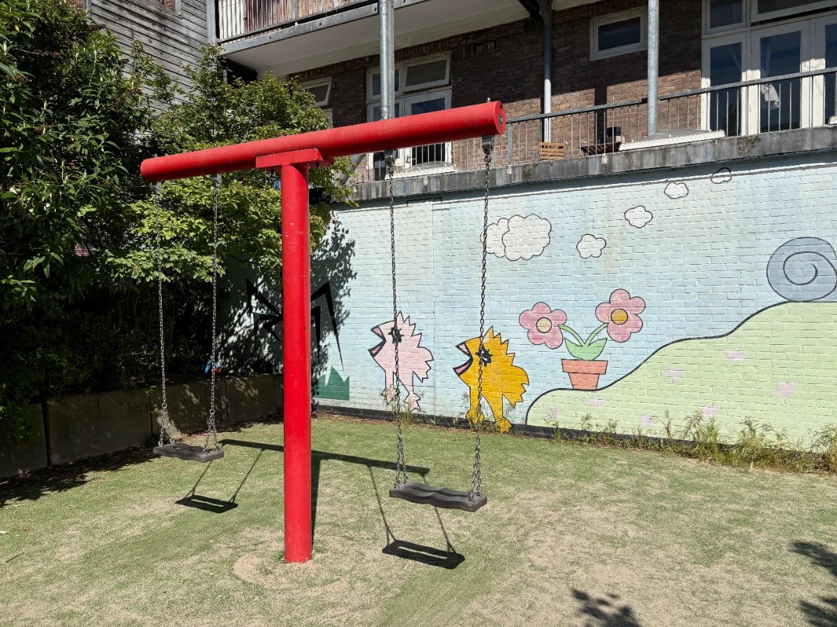 Two swings on a bright red swing set with a colorful mural behind showing chicks and flowers