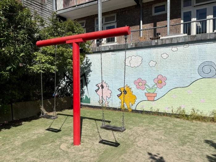 Two swings on a bright red swing set with a colorful mural behind showing chicks and flowers
