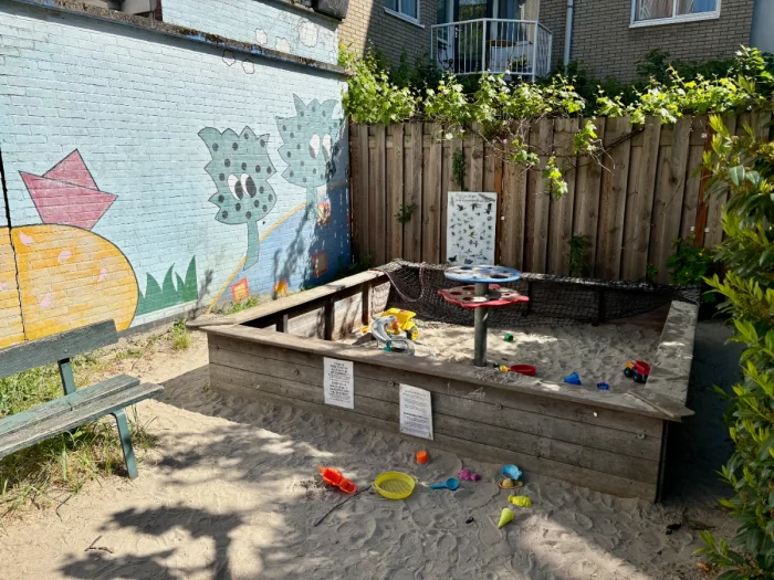 Wooden sandbox filled with toys next to a colorful mural and bench