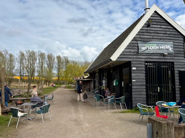 Black-painted barn with tables and chairs on the terrace and a train seen in the distance
