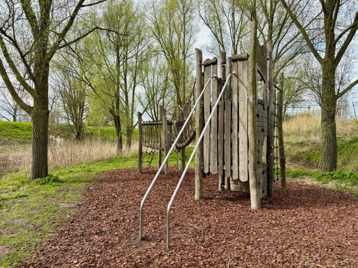 Wooden climbing structure with rope bridge and glider slide surrounded by trees