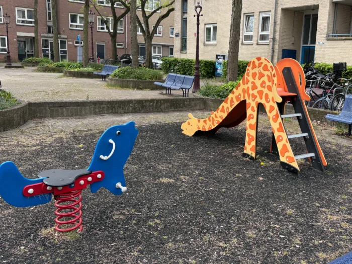 Small giraffe-shaped slide and blue seal rocker on shady playground