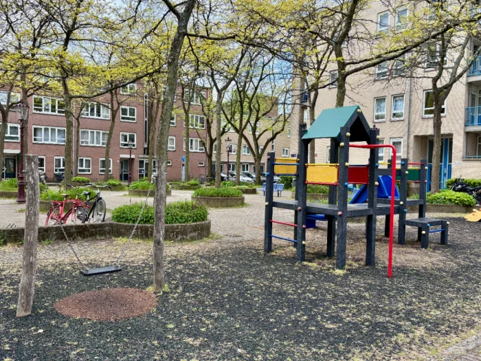 Small swing and colorful climbing structure in shady residential plaza