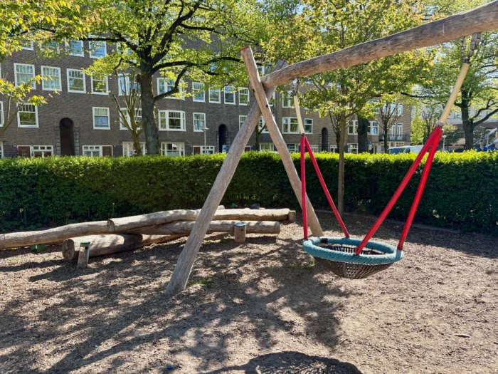 Shaded corner of a playground with nest swing and natural log climbing and balance structure