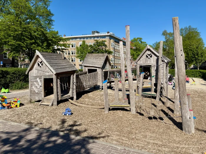 Wooden play house and obstacle course on sand with toys and trees around 