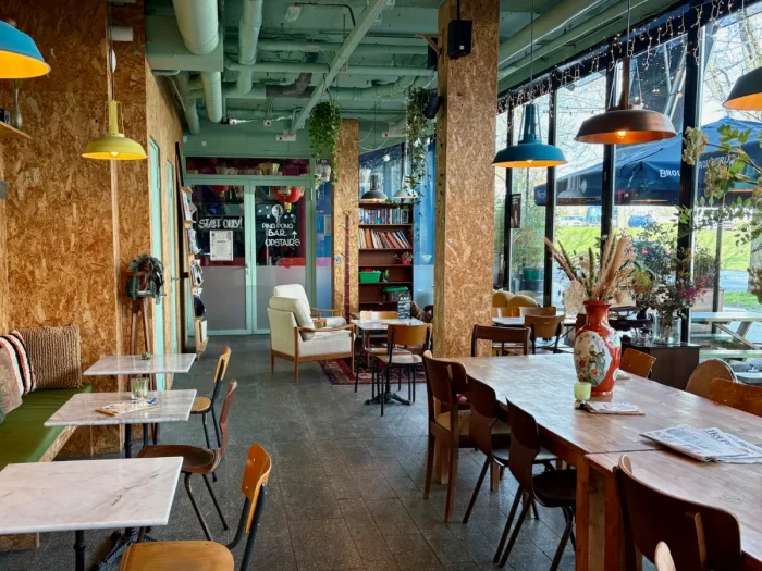 Colorful and cozy cafe with large coworking table, smaller tables with bench seating, and living-room seating area 