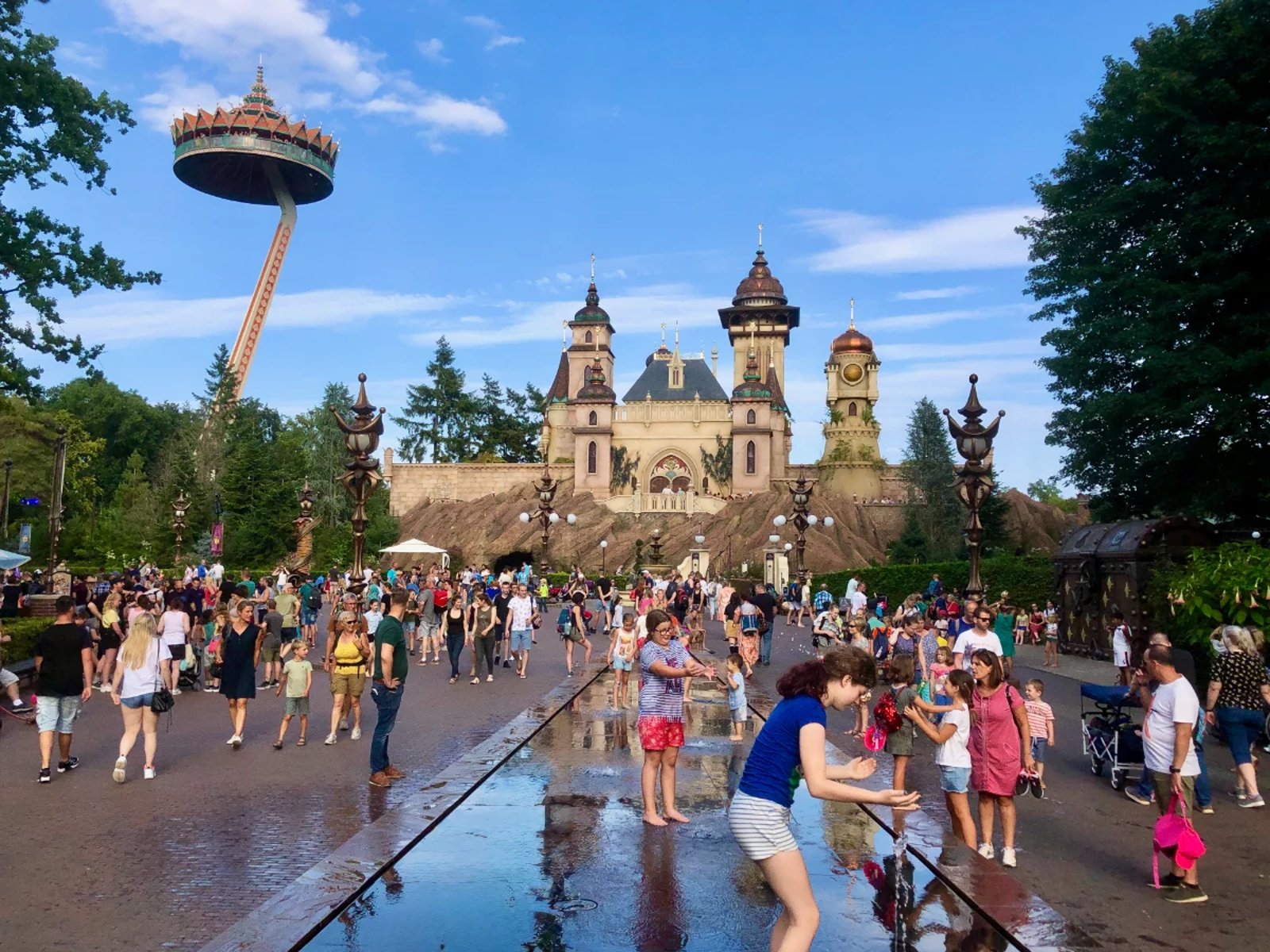 Castle at Efteling amusement park on a summer day with kids playing on splash pad and rides in the background