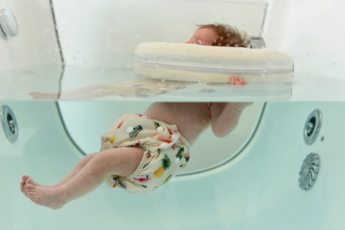 Infant floating in baby spa with colorful swim diaper and float ring around neck
