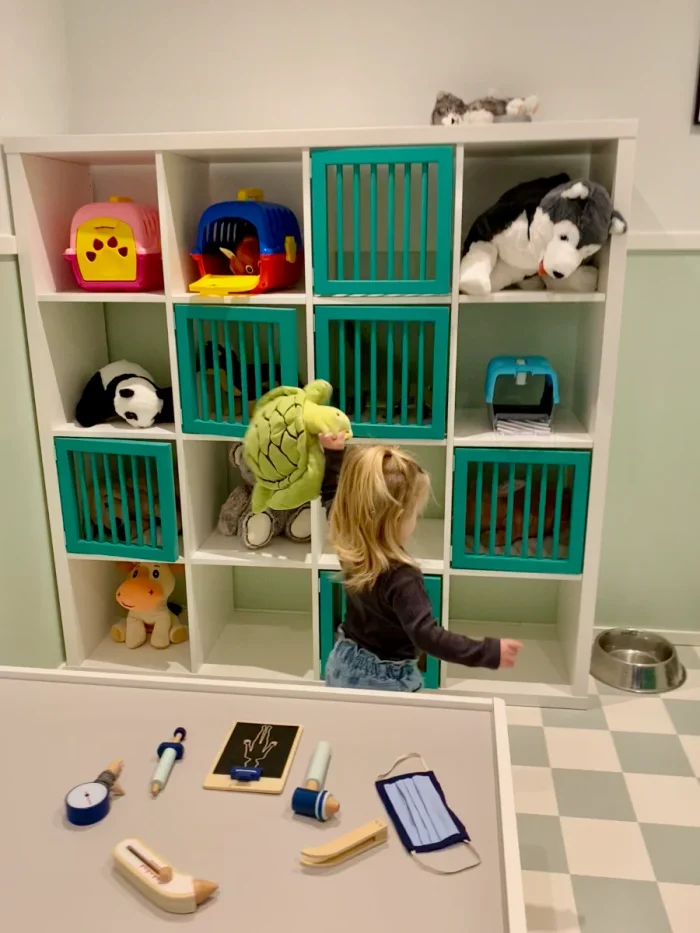 Girl playing in pretend veterinary office with wall of stuffed animals in cages and an examination table