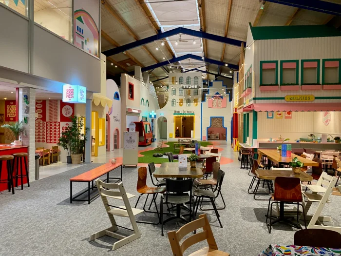 Indoor role playing village with colorful "town square" with shops, a hotel, cafes, theater and a dining area with tables and chairs near the entrance