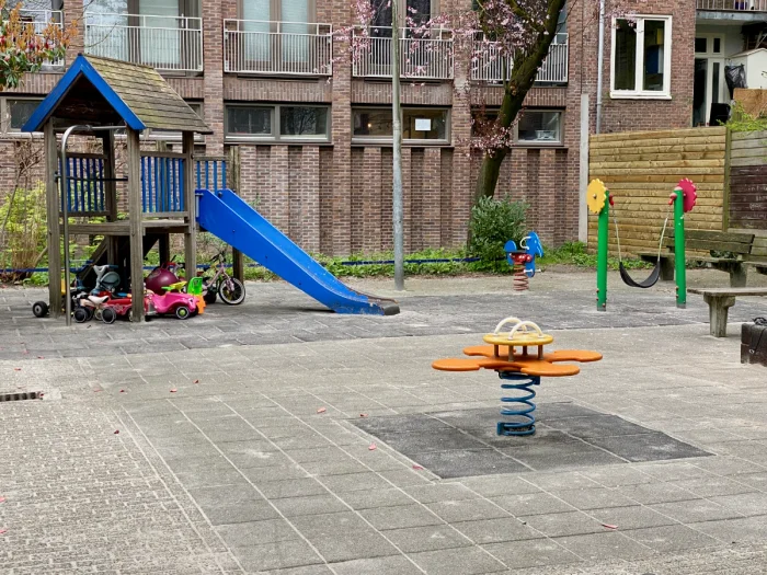 Enclosed playground with wooden house and blue slide, orange spring rocker, and green toddler swing with flowers