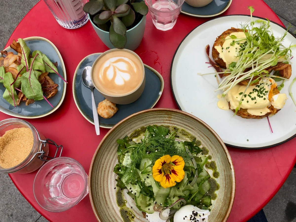 Colorful brunch dishes, latte, and jar of sugar on a bright red table