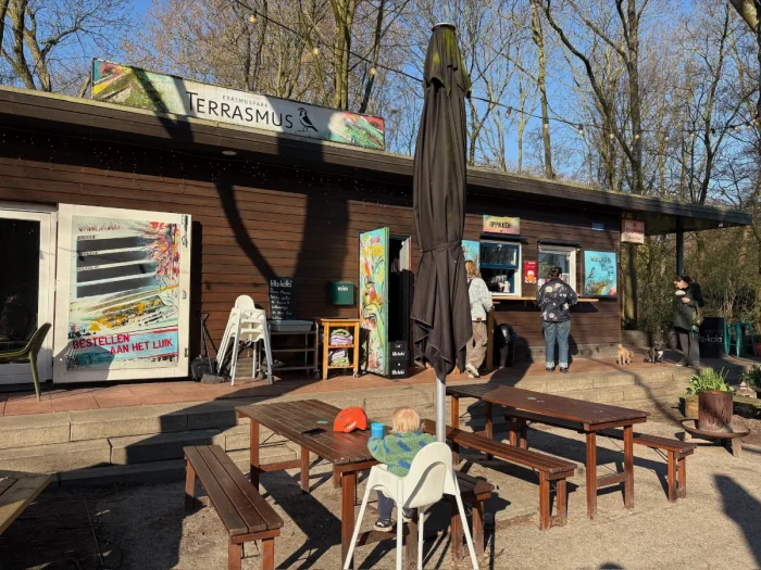Baby in a high chair by picnic benches waits while parents order snacks at a kiosk window