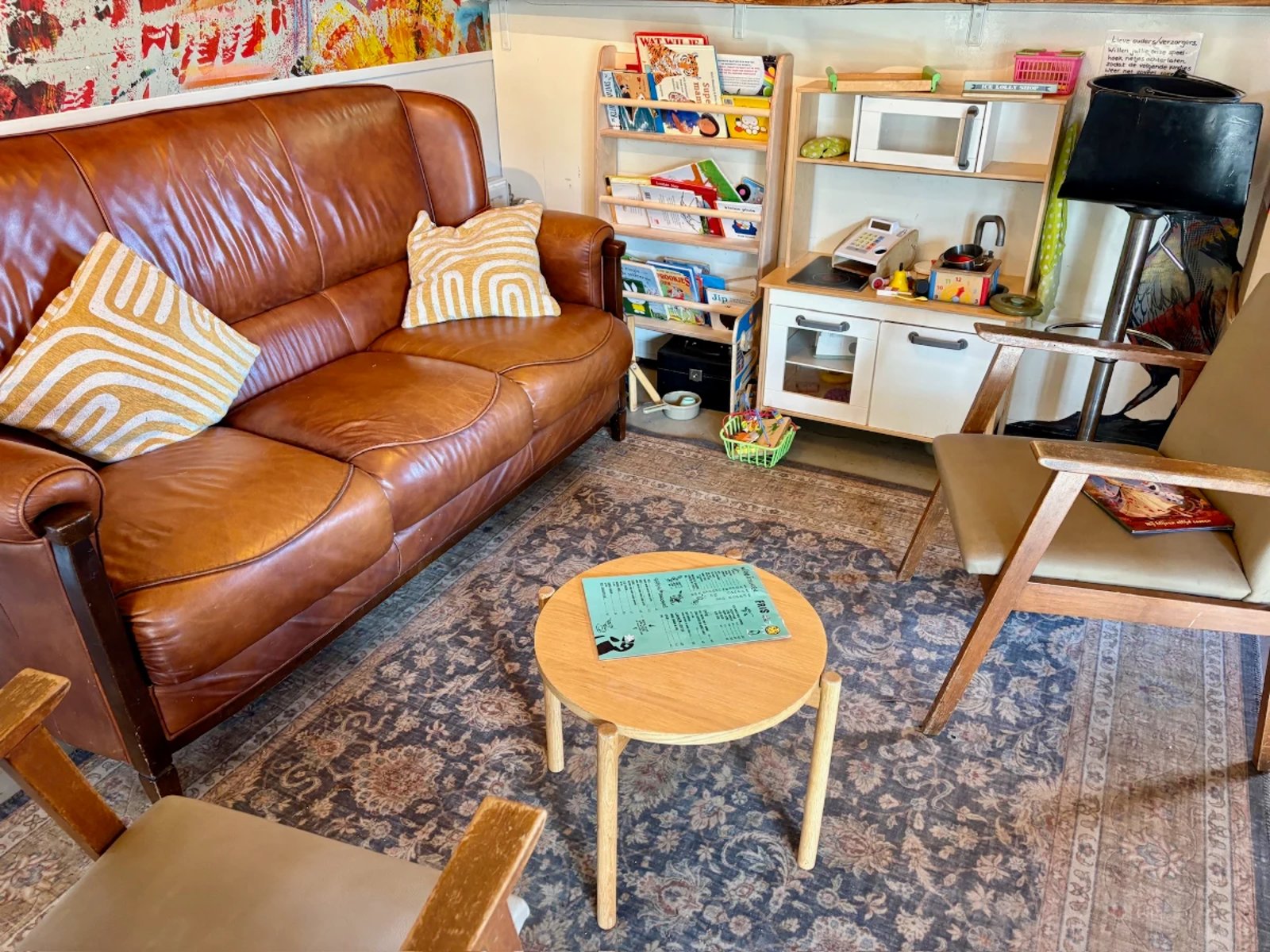 Children's play corner with play kitchen, books, toys next to seating area with brown leather couch