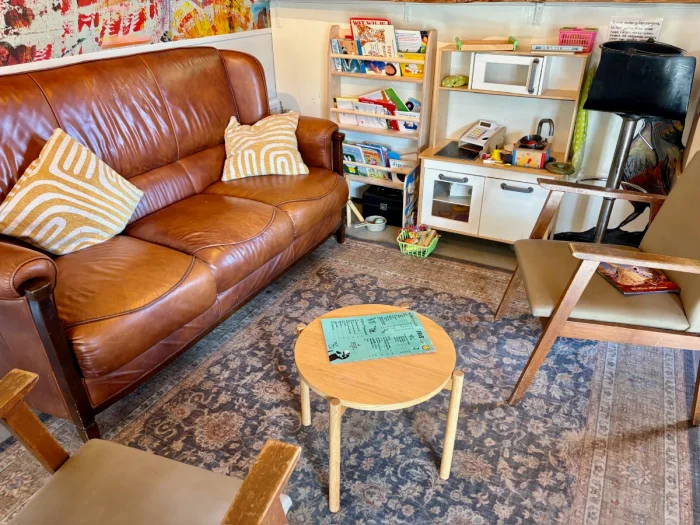 Children's play corner with play kitchen, books, toys next to seating area with brown leather couch