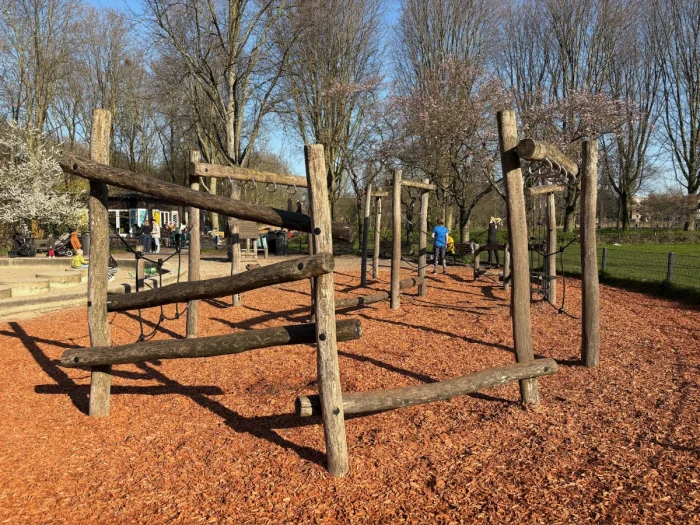 Wooden obstacle course for young kids with balance beams, ropes, monkey bars set on mulch