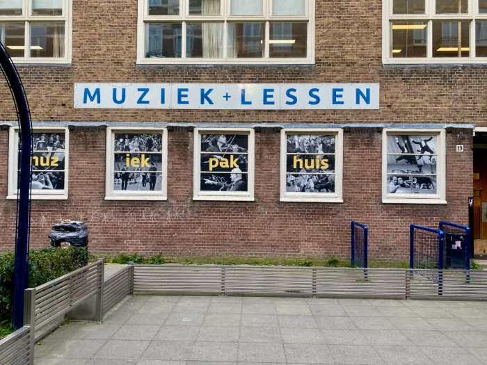 Brick building with MUZIEK LESSEN sign and black and white photos of musicians in the windows