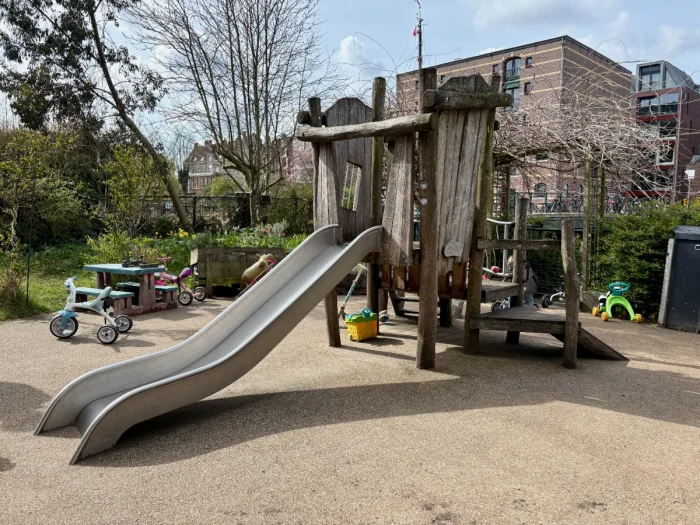 Children's playground with wooden play house with slide and several bikes and toys around