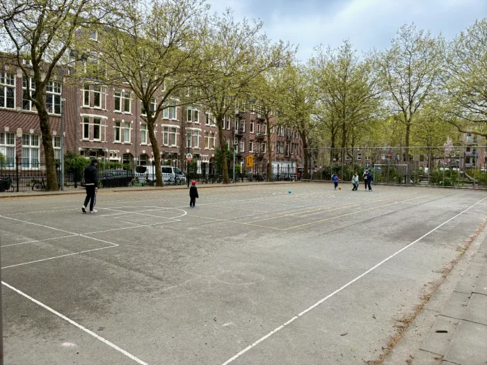 Kids playing on enclosed, paved sport court with basketball hoop and football goal and residential buildings around