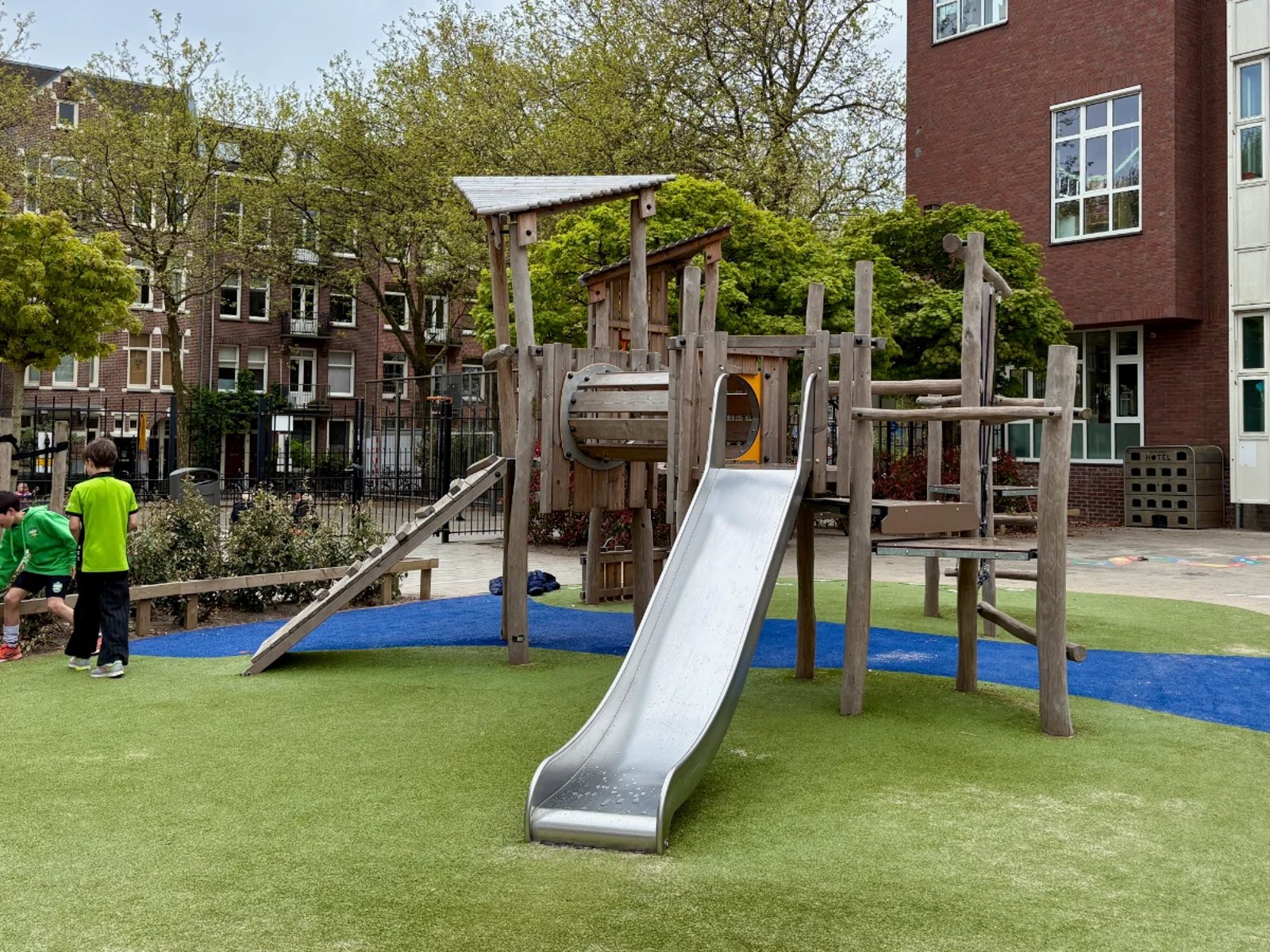 Wooden climbing structure with slide, ladders, ramp on bright green and blue astroturf