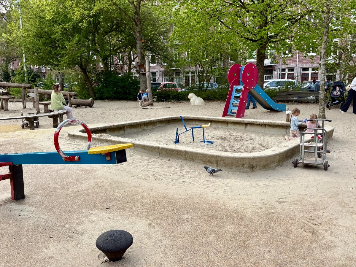 Children playing in sandbox with seesaw and red and blue slide nearby