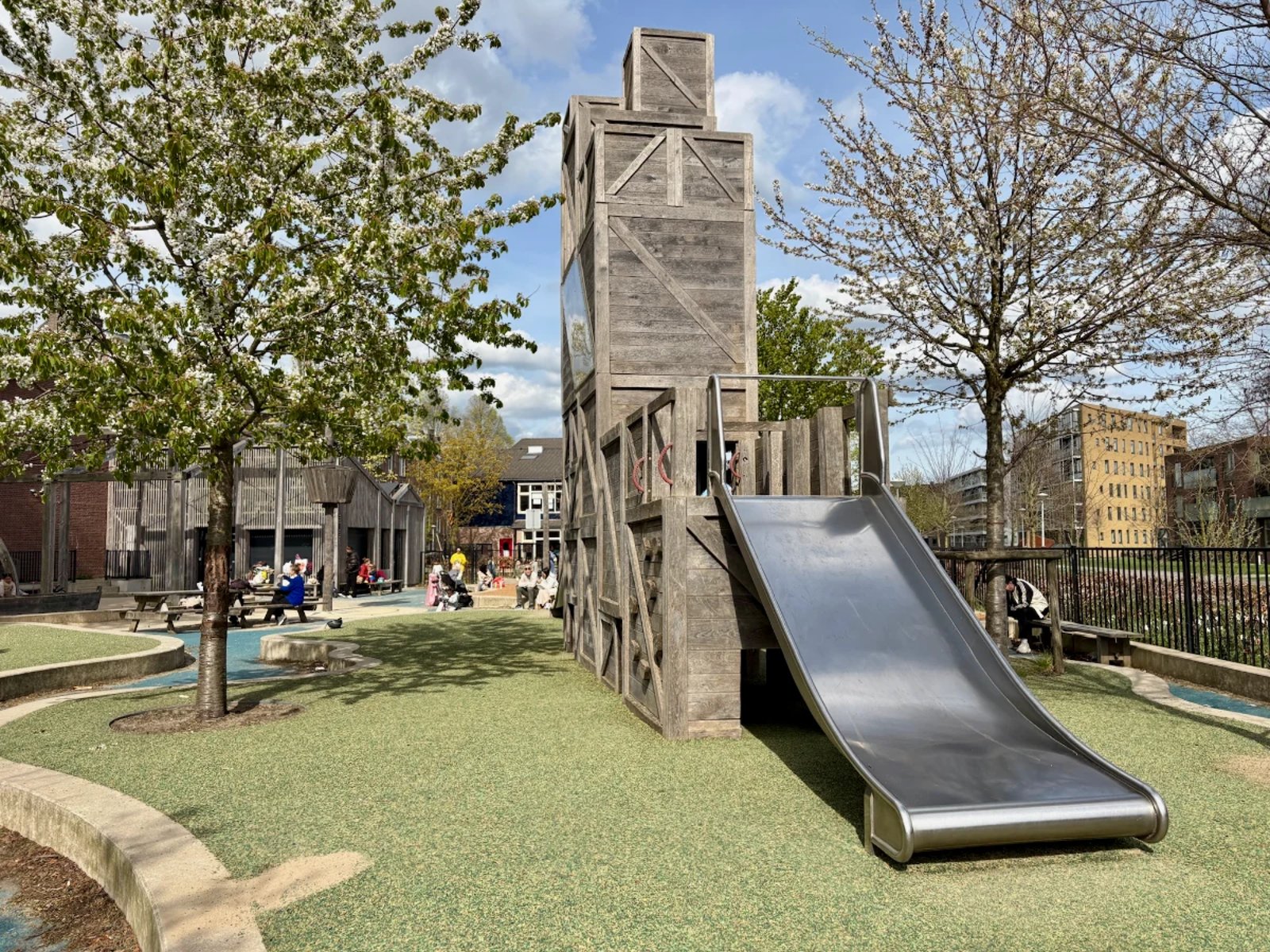 Wooden crate play tower with wide slide and community building behind
