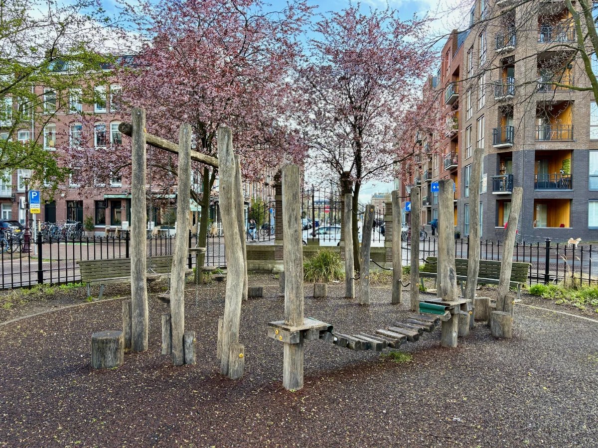 Wooden obstacle course for toddlers with ropes, bridges, stepping stones and pink flowering spring trees