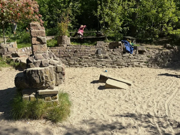Sunny sand box with rustic stone wall and trees beyond