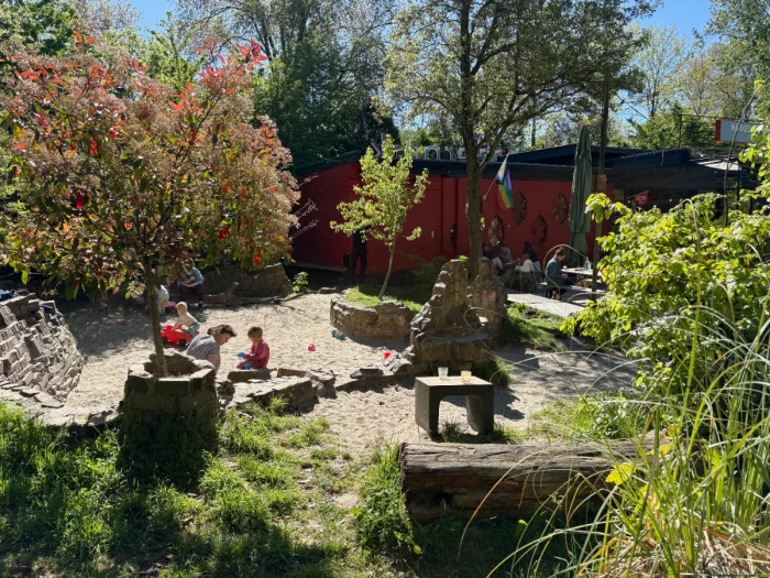 Kids playing in sunny sand box next to cafe with trees and picnic tables