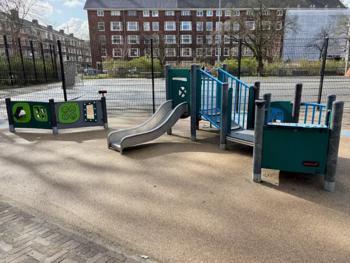 Small toddler-size play structure with slide and puzzles with enclosed soccer pitch seen behind