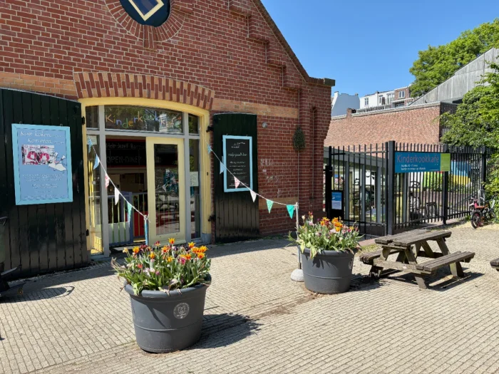 Brick cafe building with large black barn doors, bunting, flower pots, and picnic table out front