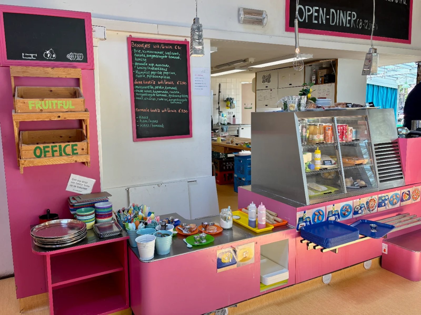 Colorful, pink kids cafe counter with children's cutlery, glass case, and chalkboard