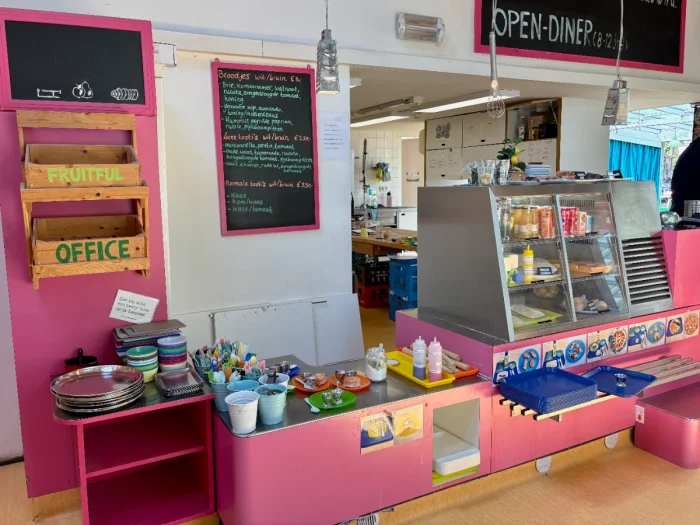 Colorful, pink kids cafe counter with children's cutlery, glass case, and chalkboard